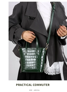 Detail of dark green crocodile pattern bucket bag with gold hardware and top handles