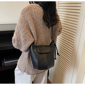 Detail of black matte leather bucket bag showing flap design and knotted shoulder strap