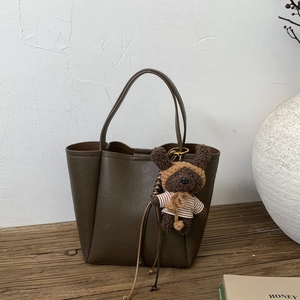 Olive green pebbled leather tote bag with a plush bear charm on a rustic wood surface