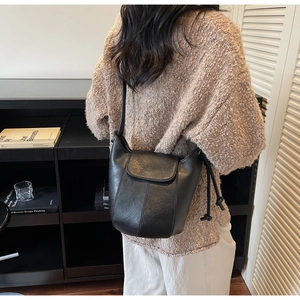 Detail of a minimalist black leather bucket bag worn by a model in a library setting