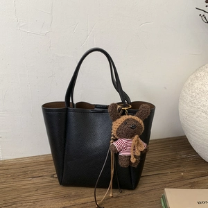 Black litchi grain tote bag with cute teddy bear charm on a wooden table setup
