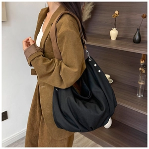 Detail view of a large black canvas tote bag with adjustable brown strap worn by a model