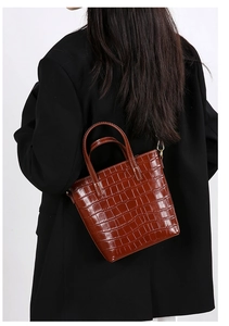 Crocodile pattern bucket bag in caramel brown worn over a black blazer by a model