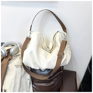 Detail of canvas hobo bag with wide brown straps and silver buckles in a lifestyle setting