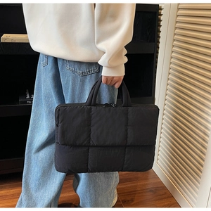 Detail of black quilted laptop bag featuring padded diamond texture and dual zipper closure