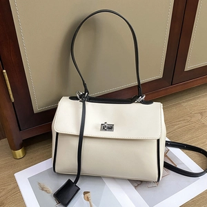 Minimalist cream bucket bag with black contrast trim and silver turn-lock on wood floor