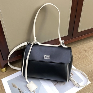 Minimalist black bucket bag with contrast white trim and silver twist lock on wood floor