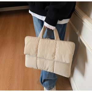 Detail of beige quilted puffer handbag in hand showing soft nylon texture and dual handles