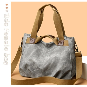 Detail of grey canvas tote bag featuring brown leather reinforcement and sturdy metal hardware