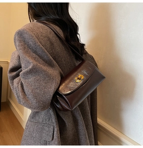 Detail of vintage brown leather underarm bag with gold metal buckle on female shoulder