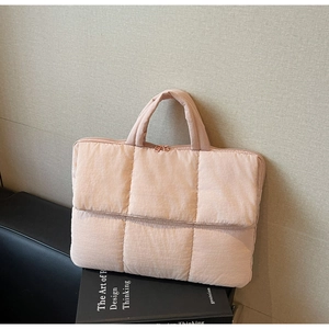 Close-up of pink quilted puffer laptop sleeve with cylindrical handles on a book