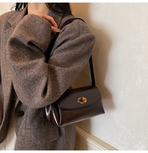 Detail of a dark brown glossy shoulder bag with a gold twist lock on a vintage blazer