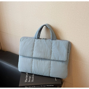Detailed quilted texture of light blue laptop sleeve with handles on decorative books