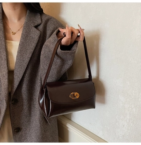 Detail of a dark brown vintage shoulder bag with a gold oval twist lock on a grey blazer