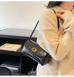 Detail of black glossy faux leather shoulder bag featuring a round golden metallic lock