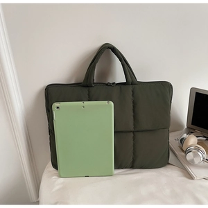 Detail of dark green quilted laptop bag showing padded texture and dual metal zippers