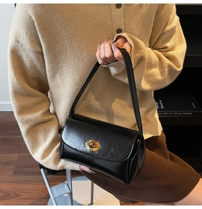 Detail of glossy black vintage handbag featuring a gold oval twist lock and faux leather