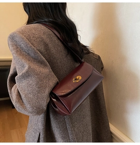 Detail of burgundy leather shoulder bag with golden oval clasp on a wool blazer