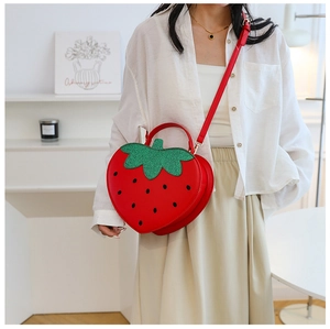 Detail of red strawberry-shaped crossbody bag with green leaf handle shown on a model