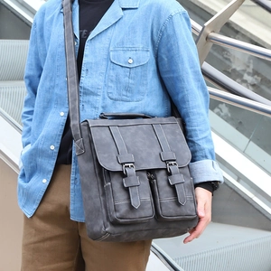 Men's dark gray messenger bag with double buckles and stitching in an outdoor setting