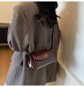 Detail of dark wine red leather shoulder bag with gold metal clasp on a textured blazer