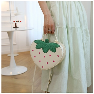 Close-up of a strawberry-shaped crossbody bag featuring white faux leather and green glitter leaves