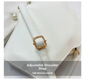 Detail of adjustable leather shoulder strap with gold buckle on a white handbag