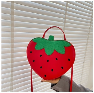 Close-up of red strawberry shaped crossbody bag with green leaf decor and strap