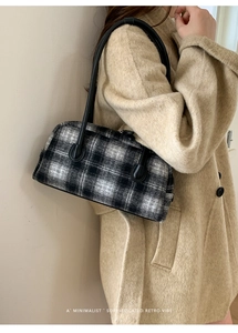 Detail of a black and white plaid Boston bag held by a model in a beige coat