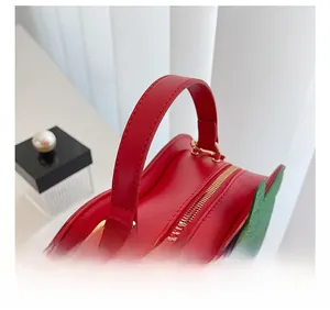 Detail of red strawberry bag featuring wide handle, gold hardware, and green leaf accent