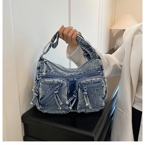 Détail d'un sac à main en denim bleu clair avec plusieurs poches zippées en métal
