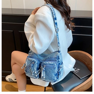 Détail du sac bandoulière en denim délavé avec poches multiples et fermetures argentées