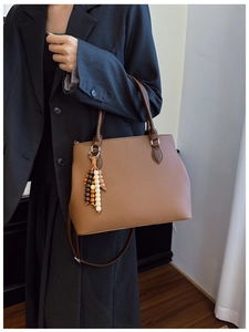 Detail of a brown leather tote bag with a unique wooden bead charm and crossbody strap