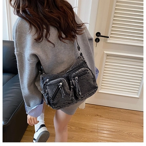 Détail du sac à bandoulière en jean gris avec poches zippées et pompons porté par un mannequin