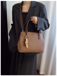 Brown lychee grain tote bag with wood bead tassel, styled on shoulder with gray suit