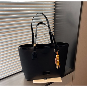 Detail of black leather tote bag with metallic brand plate and colorful beaded charm