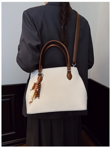 Detail of white lychee grain tote bag with brown handles and beaded tassel accessory