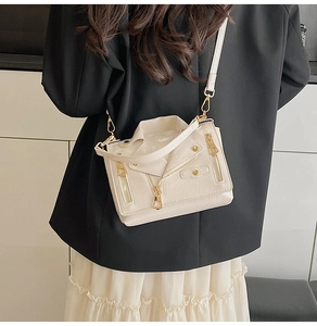 Detail of a beige biker jacket shaped crossbody bag with metal zippers and stud accents