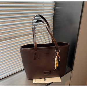 Detail of vintage brown leather tote bag featuring a boho beaded tassel and logo plaque