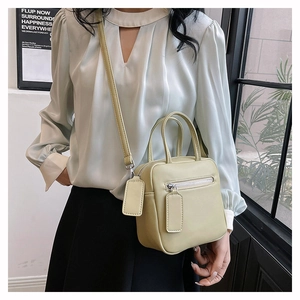 Detail view of avocado green crossbody bag with dual handles and stylish front zipper pocket