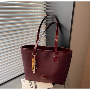 Detail of burgundy leather tote bag with glossy straps and bohemian beaded charm