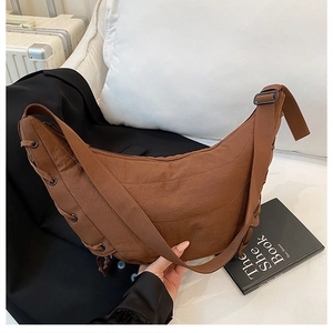 Close-up of a brown croissant bag with tied ribbon details and adjustable wide shoulder strap