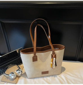 Detail of canvas tote bag with brown leather trim and colorful beaded charm accessory