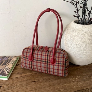 Cylindrical retro plaid shoulder bag with red leather handles on a wooden table
