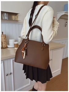 Close-up of brown lychee texture tote bag with a decorative beaded tassel charm
