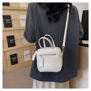 Close-up of white leather crossbody bag showing dual handles and front zipper pocket detail
