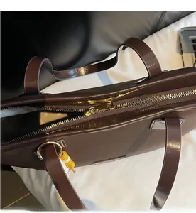 Detail of smooth gold zipper closure and herringbone lining on brown leather tote bag