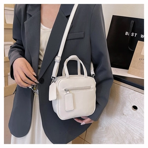 White leather crossbody square bag with dual handles and adjustable strap on a grey suit model