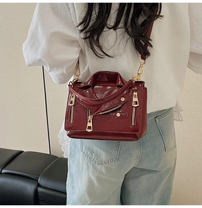 Detail of burgundy patent leather crossbody bag with motorcycle jacket design and gold zippers