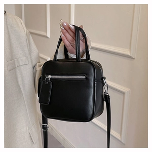 Close-up of minimalist black small square bag featuring silver hardware and side zippers
